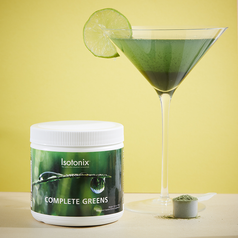 Isotonix Complete Greens, with a serving scoop filled with powder product, and a martini glass with a lime wedge, filled with green liquid