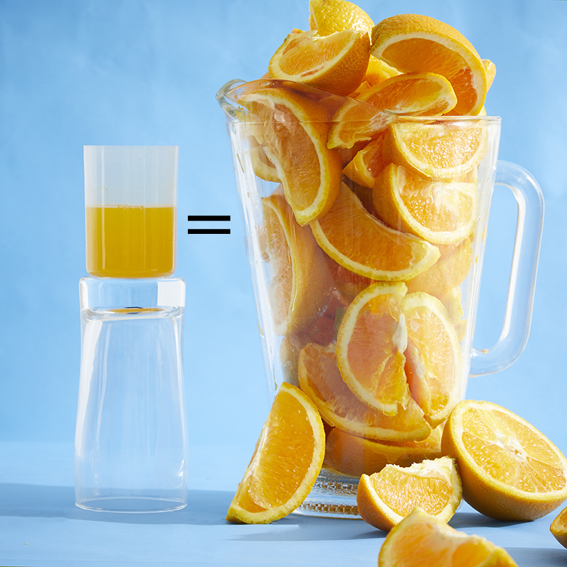 Isotonix Vitamin C, with liquid serving cup partially filled, sitting on an upside down glass next to a pitcher overflowing with sliced oranges