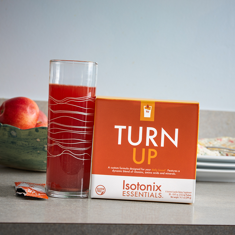 Isotonix Essentials Turn Up showing open packet, glass containing mixed product and a bowl of apples