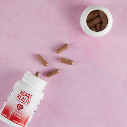 Heart Health Blood Pressure and Vascular Support capsules spilled onto pink table next to an open bottle of the same