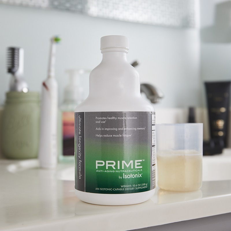 Prime Ultimate Longevity Formula by Isotonix®, with liquid serving cup partially filled, on bathroom sink with tooth brushes