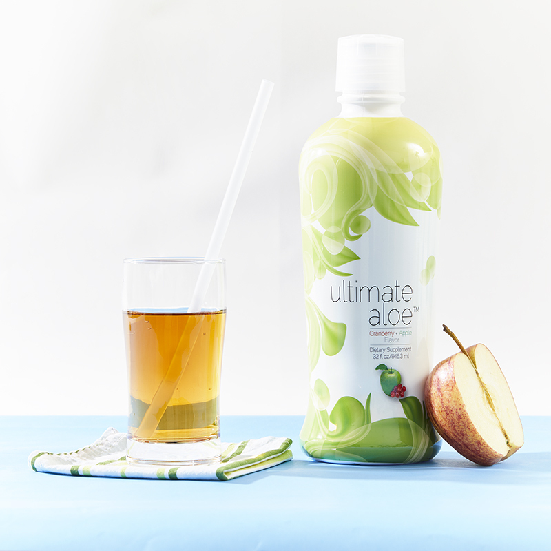 Ultimate Aloe Cranberry Apple Flavor, a mostly filled glass with a straw, and half an apple
