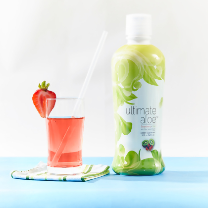 Ultimate Aloe Strawberry Kiwi Flavor, with a glass almost filled with liquid, a strawberry on the brim, and a straw, on a folded towel