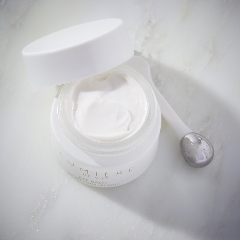 Lumière de Vie Eye Balm, jar opened showing white cream, with applicator next to it.
