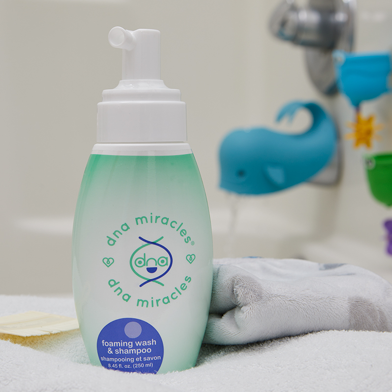 DNA Miracles Natural Foaming Wash & Shampoo pump bottle, on a bath tub with folded towels and toys in background