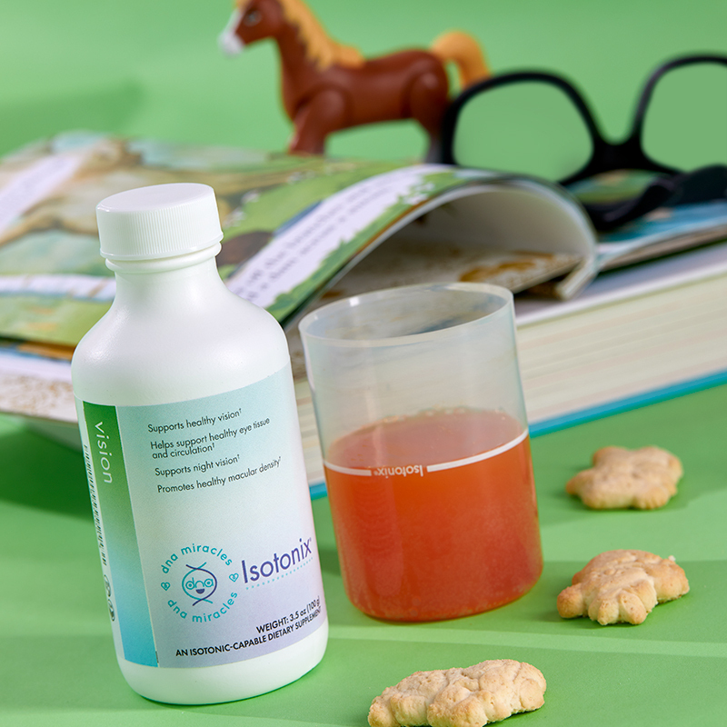 DNA Miracles Isotonix Vision, with liquid serving cup partially filled, a story book, animal crackers, and toy horse and eyeglasses in the background