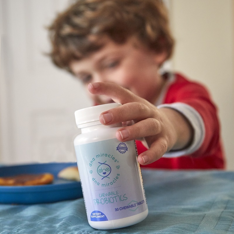 DNA Miracles Chewable Probiotics bottle held out by a child, with a blue plate of food nearby