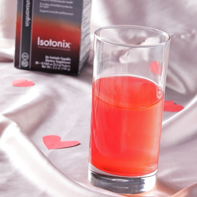 Isotonix Astaxanthin, product box in background, glass contains product mixed with water, sitting on a silk background