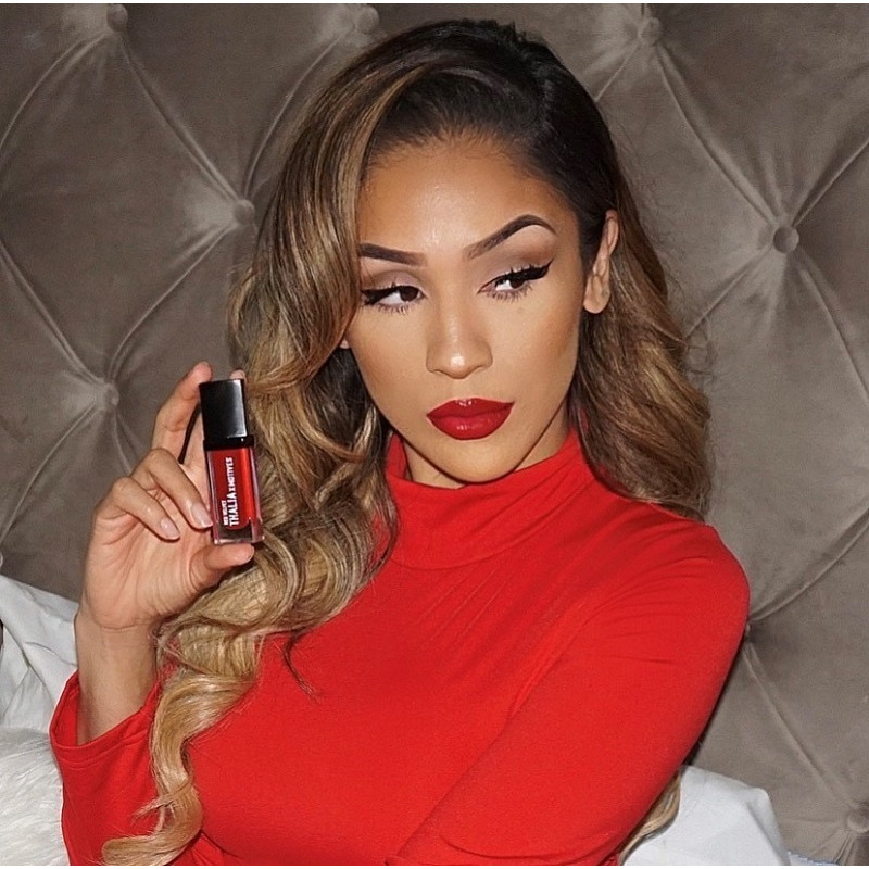 Woman wearing Red holding THALIA X Motives Liquid Lipstick in Red Velvet, looking to her side