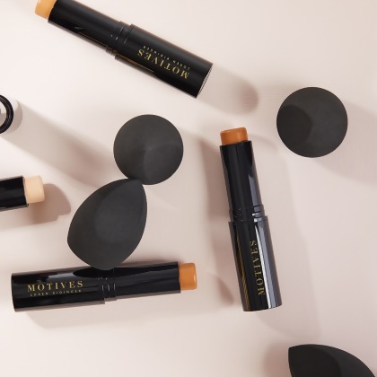 Motives Blending Sponges shown with Motives Foundation Sticks on a cream colored table