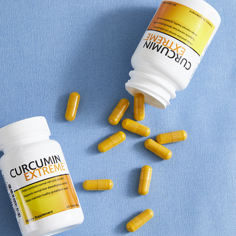 Curcumin Extreme bottles, with yellow-orange caplets poured on a blue table to view