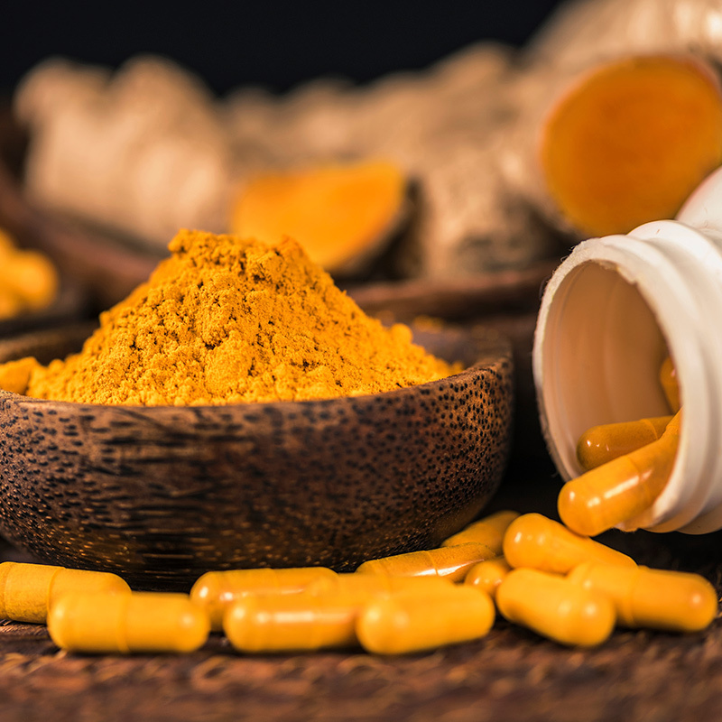 Curcumin Extreme capsules with Curcumin yellow-orange powder poured into a bowl 