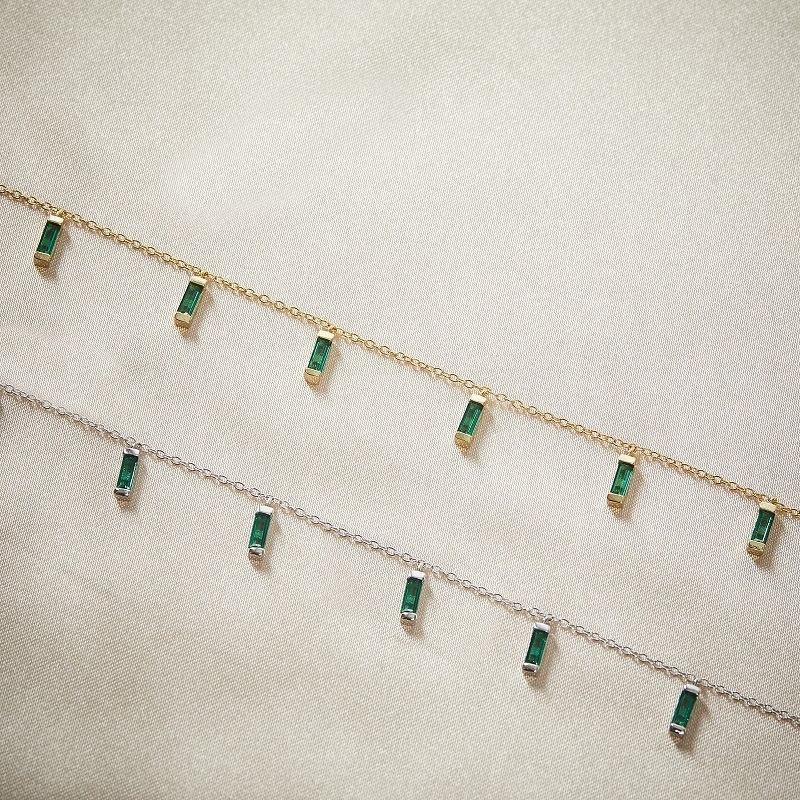Closeup of 2 Layered CARYN - Emerald Green Baguette Drop Necklaces, with green stones, one in gold and one in silver