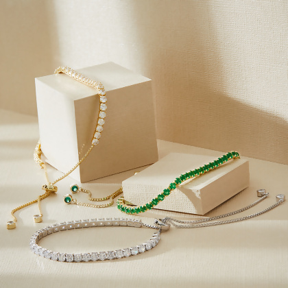 Three Layered VIOLET - Round Cut Tennis Bracelets, silver and gold bracelets with clear gems, and gold with green gems, on a display box