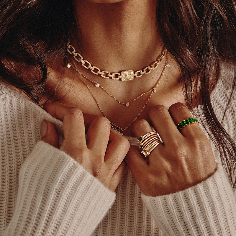 Model wearing 8 Layered Adrienne - Spiraled Baguette Rings, stacked, with green stones and clear stones, in gold, with other rings and necklaces