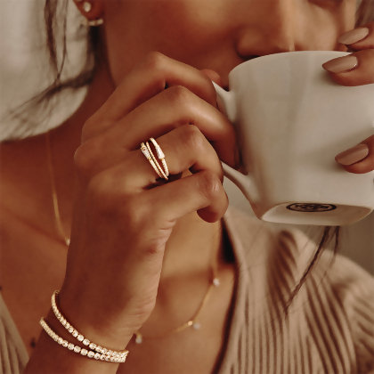 Model wearing Layered Adrienne - Spiraled Baguette Rings, stacked, with clear stones in gold, with other Layered bracelets, drinking coffee