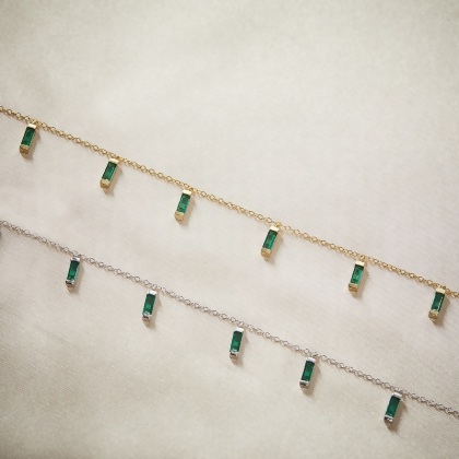 Closeup of 2 Layered CARYN - Emerald Green Baguette Drop Necklaces, with green stones, one in gold and one in silver