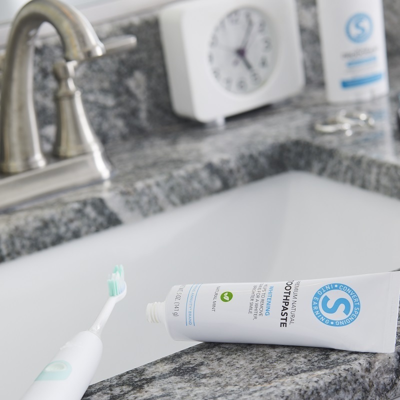 Shopping Annuity Brand Premium Natural Toothpaste on a sink with a toothbrush clock and mouthwash.