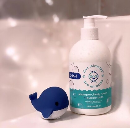 DNA Miracles 3-in-1 Shampoo, Body Wash + Bubble Bath, sitting on the side of a bathtub with a toy whale