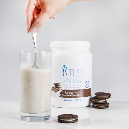 TLS Nutrition Shakes - Cookies & Cream, being stirred in a glass with a spoon with cookies stacked to the right