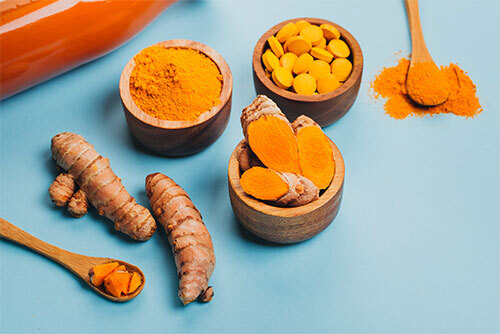 Turmeric roots in wooden bowls and spoons.